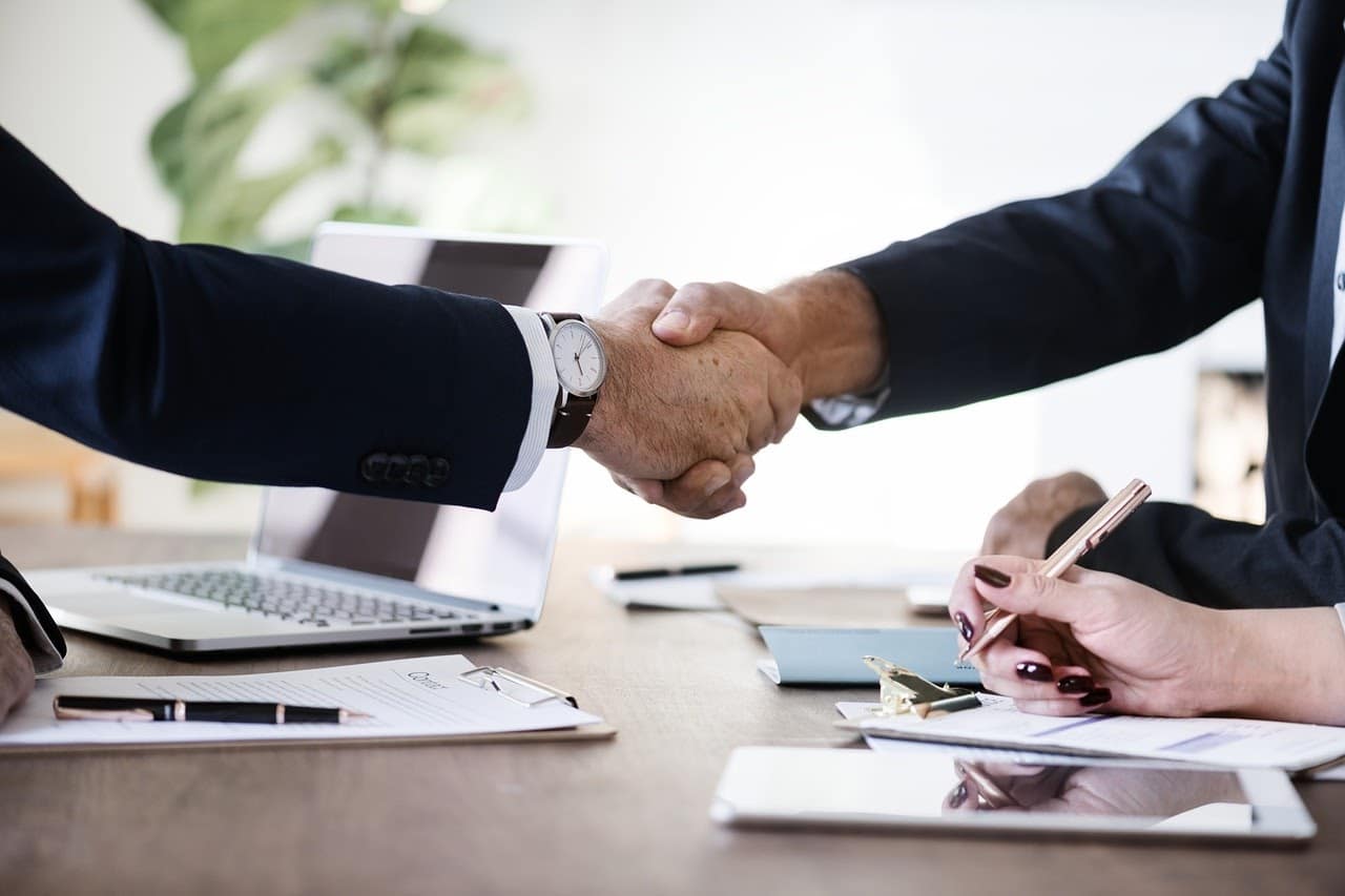 Two people in business attire shaking hands over an office desk.