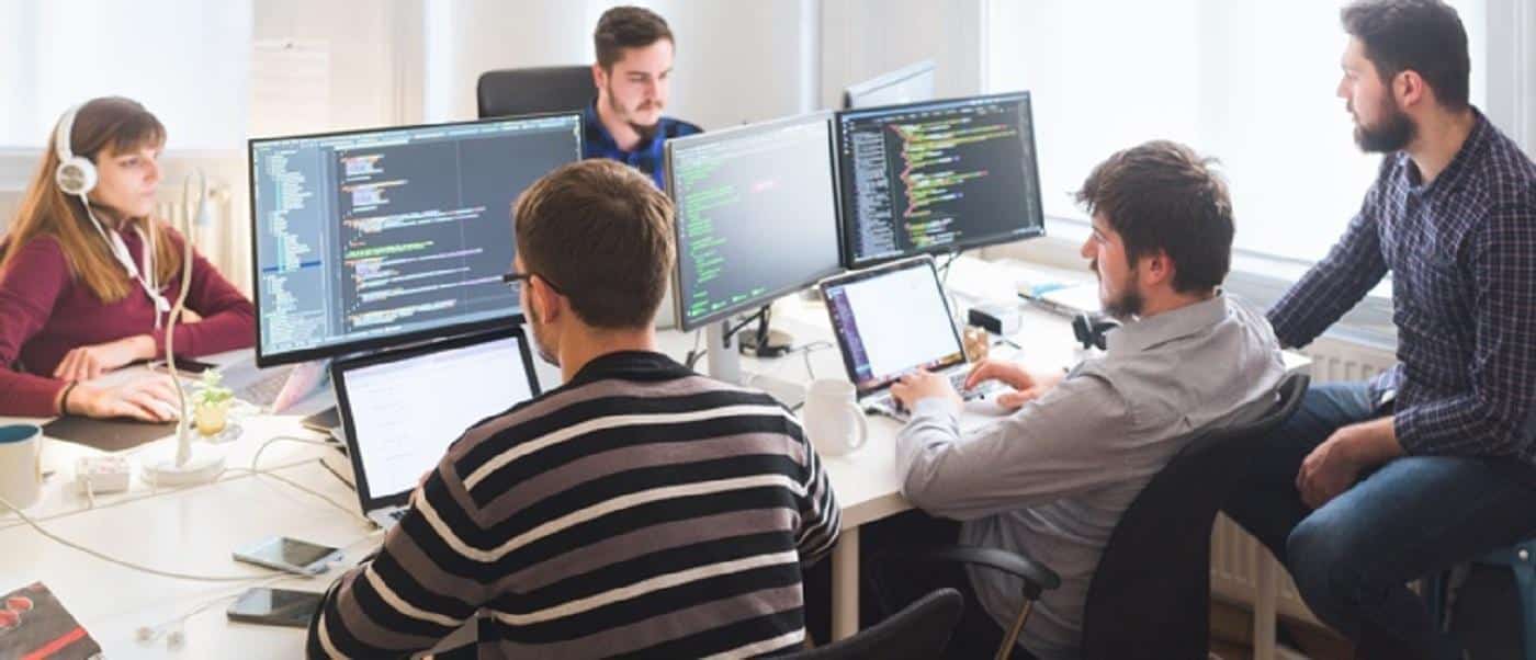 Un gruppo di persone che lavorano di fronte al computer, sui loro schermi si vedono delle pagine di editor di codice. 