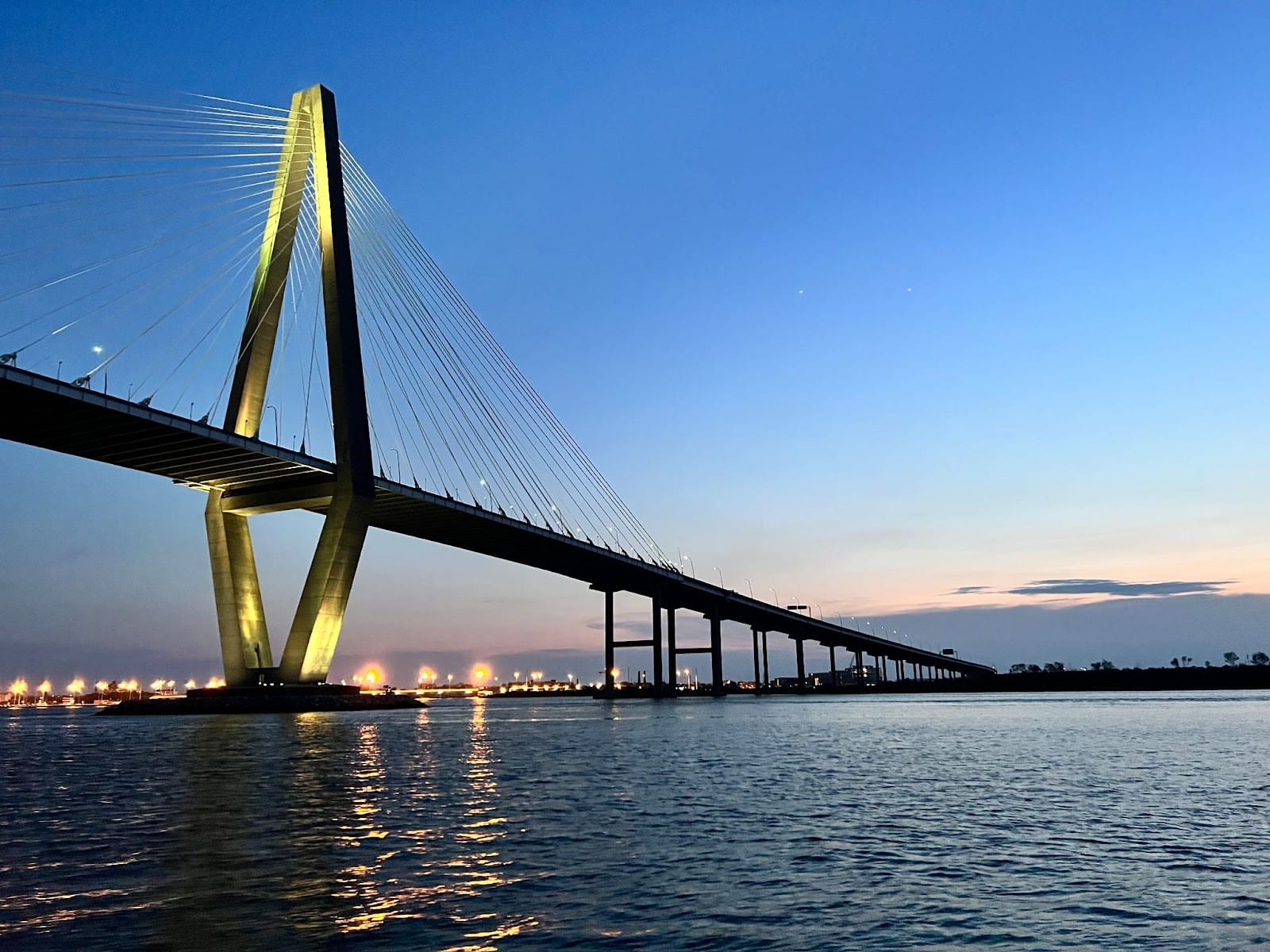 Un moderno puente colgante iluminado sobre un río al atardecer.