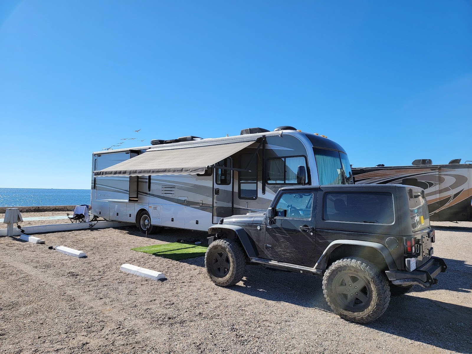 A Jeep and an RV parked next to each other in a parking lot with a view of the ocean..